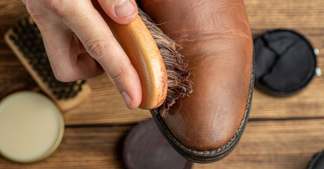 A man uses a horsehair shoe brush to apply shoe polish to a brown leather boot to restore its finish and shine.