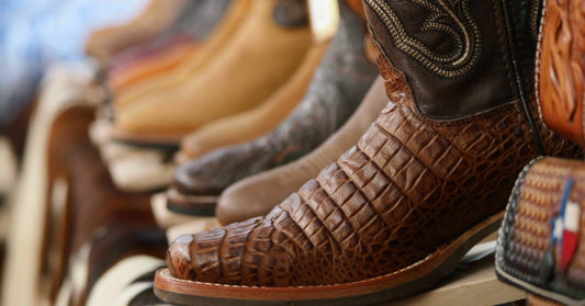 A store shelf with boots in various shades of browns, blacks, and tans, that have smooth and exotic leather.